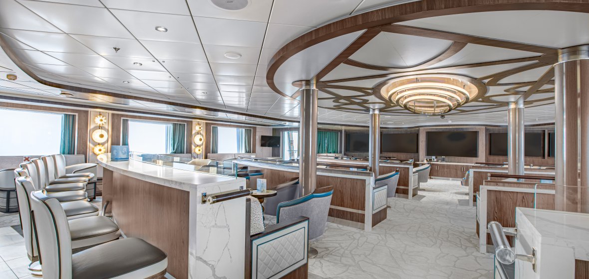 Luxury Cruise Ship Lecture Room with Modern Design An elegant and spacious lecture room or lounge aboard a luxury cruise ship, featuring curved wood paneling, marble-topped counter seating, plush upholstered chairs in neutral tones with teal accents, and sophisticated ceiling details with circular lighting fixtures. Large panoramic windows provide ocean views, creating a refined atmosphere for onboard entertainment and gatherings.