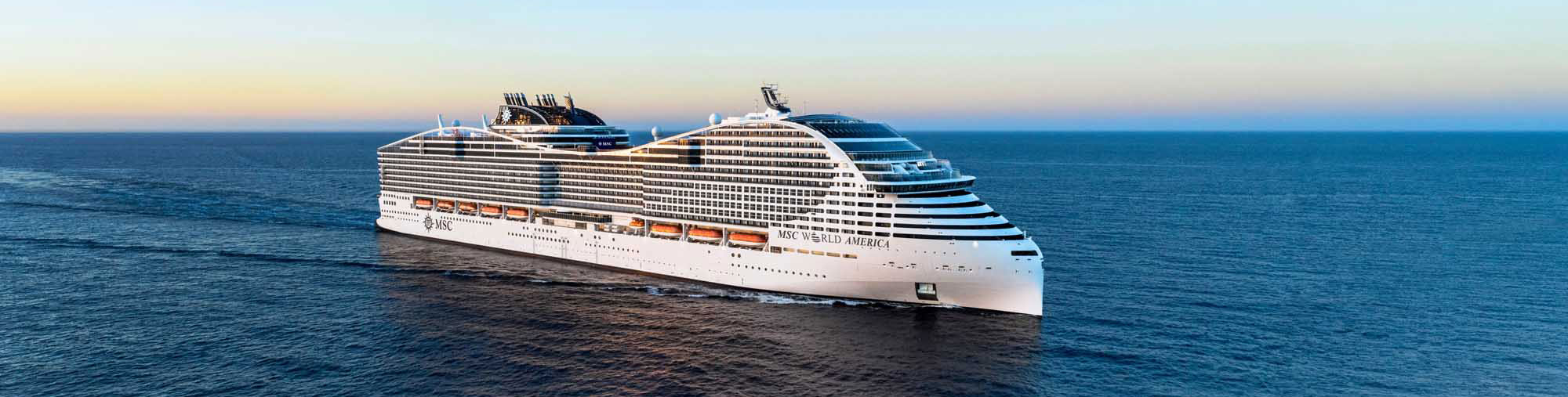MSC World America Cruise Ship at Sea A massive modern cruise ship, the MSC World America, sails through calm blue waters during golden hour. The vessel displays the distinctive MSC livery with its characteristic blue and white hull, multiple decks, and prominent funnel, representing one of the largest ships in the cruise industry.