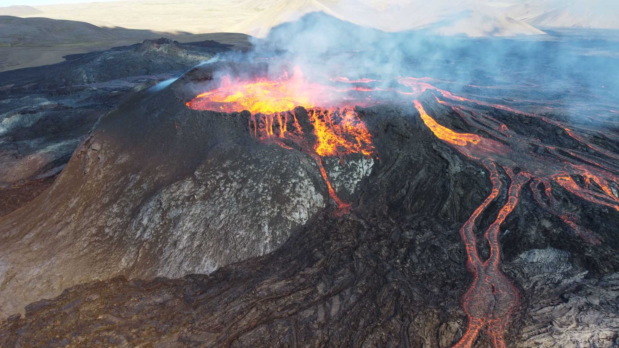 Mauna Loa Volcano Active Lava Eruption A dramatic aerial view of Mauna Loa volcano in Hawaii during an active eruption, with glowing lava fountains and flowing streams of molten rock cascading down the volcanic slopes, surrounded by dense volcanic rock formations and plumes of volcanic gases rising into the sky.