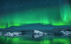 Northern Lights Over Jökulsárlón Glacier Lagoon A stunning display of vibrant green aurora borealis dancing across the night sky above a glacial lagoon filled with floating icebergs, creating a magical Arctic landscape with mirror-like reflections on the water below.