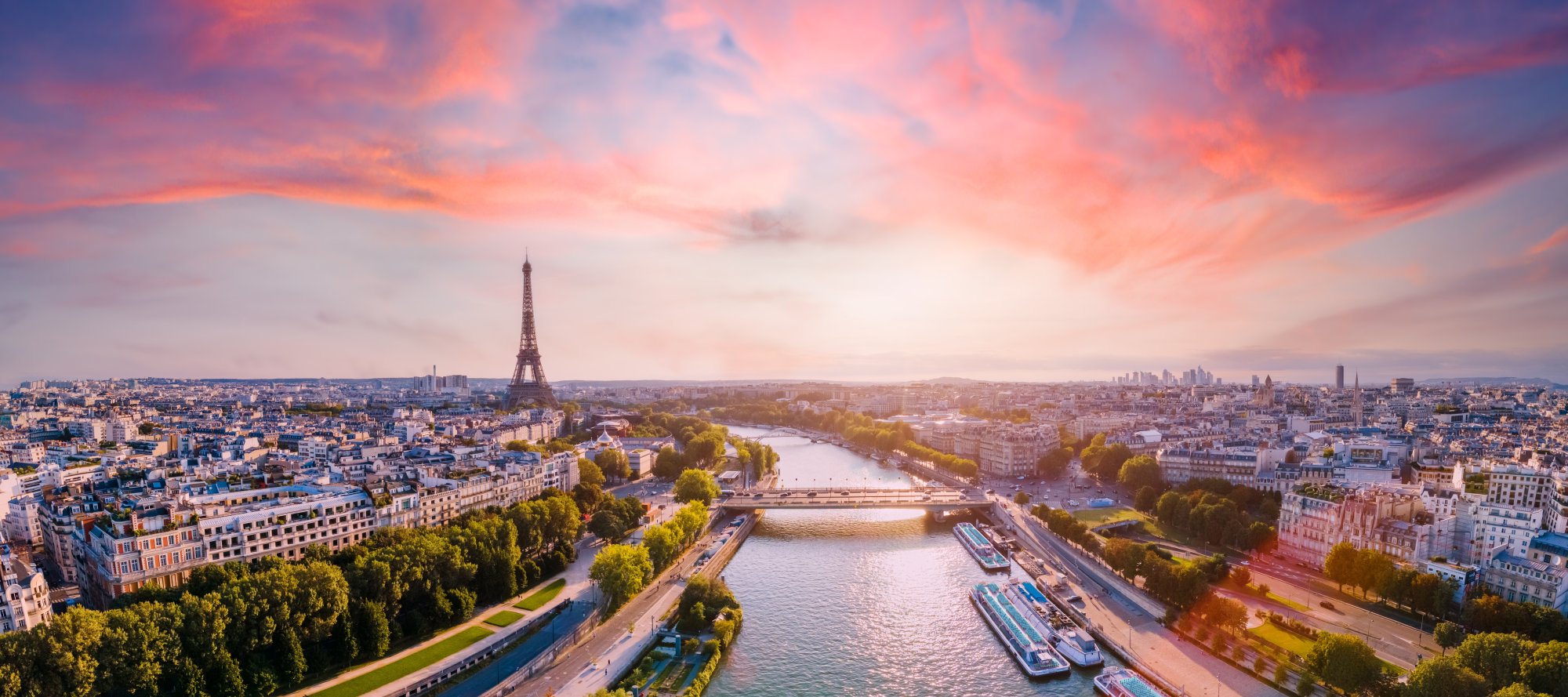 Paris Skyline at Sunset with Eiffel Tower An aerial view of Paris at golden hour, featuring the iconic Eiffel Tower prominently in the center, with the Seine River winding through the cityscape, historic Haussmann-style buildings, and vibrant pink and orange sky reflecting off the water. This breathtaking sunset panorama captures the romantic essence of the French capital.