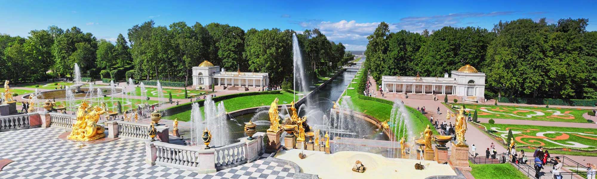 Peterhof Palace Golden Fountains and Gardens An aerial view of the magnificent Peterhof Palace complex featuring elaborate golden sculptural fountains, geometric formal gardens, cascading water features, and neoclassical pavilions with golden domes, surrounded by verdant parkland and tree-lined avenues in Russia.