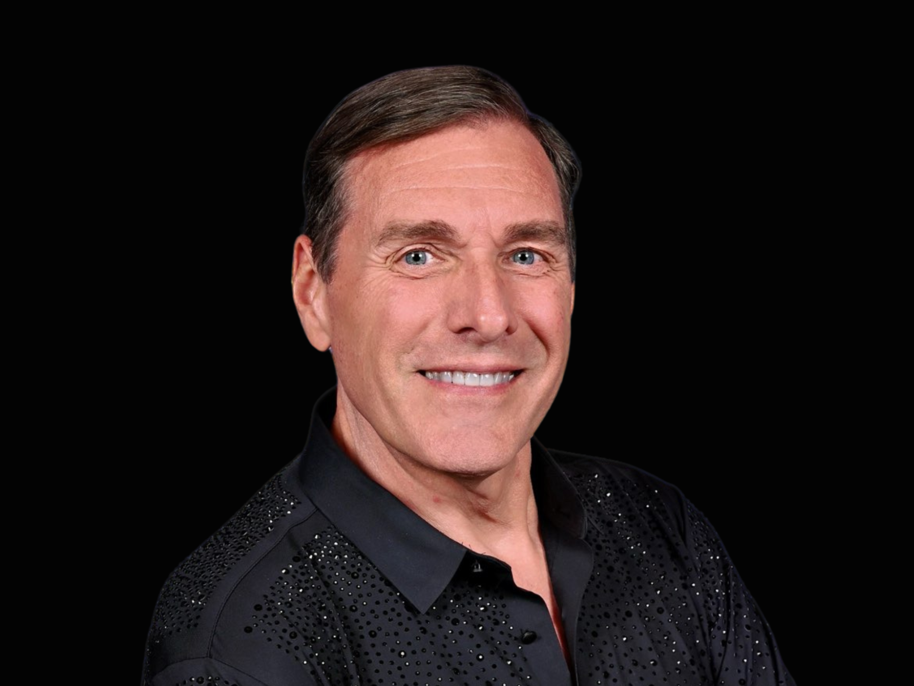A professional portrait photograph of a middle-aged man with a warm smile, wearing a black