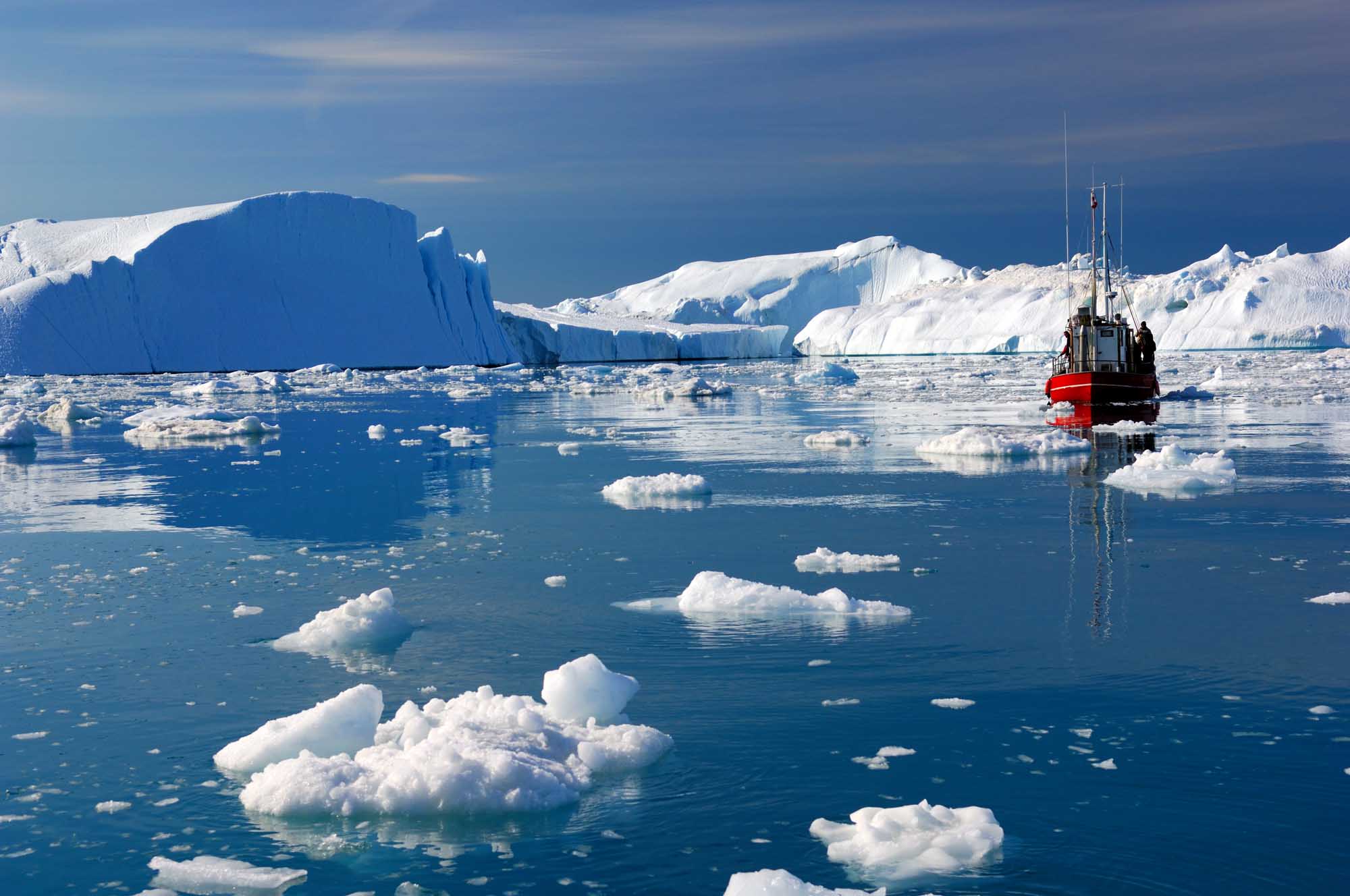 Research Vessel Among Greenland Icebergs A red and black research vessel navigates through icy waters surrounded by massive tabular icebergs and smaller ice floes in Disko Bay, Greenland. The pristine Arctic landscape features dramatic ice formations and bright blue water under clear skies.