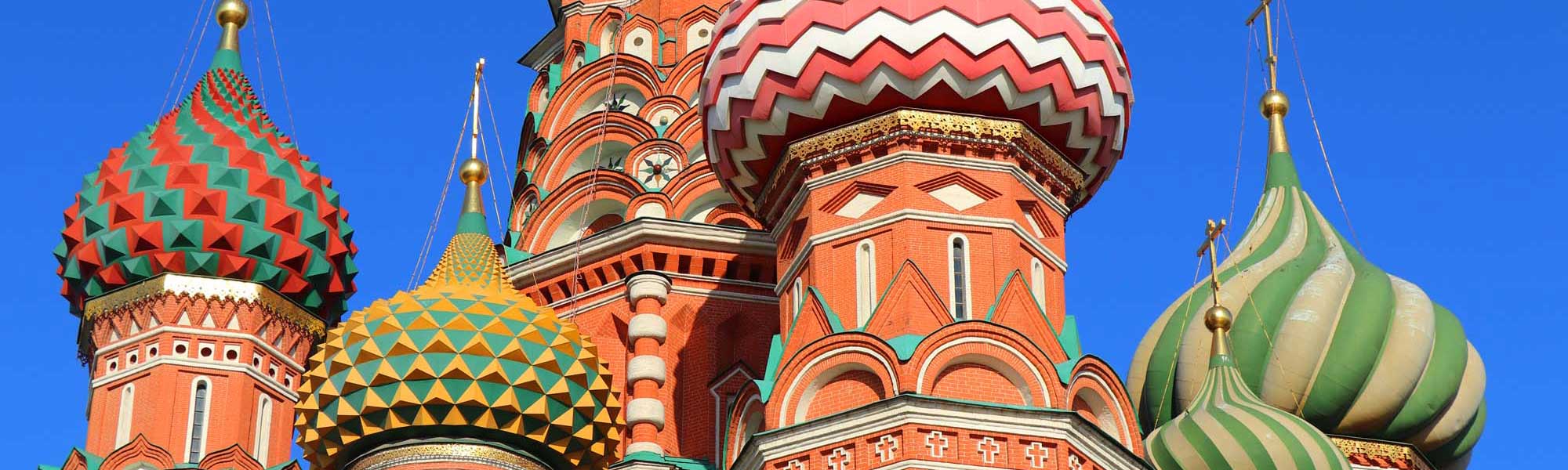 Russian Orthodox Church with Colorful Onion Domes A striking Russian Orthodox church featuring distinctive colorful onion domes with intricate geometric patterns in red, green, gold, and white against a clear blue sky. The ornate architecture showcases traditional Russian ecclesiastical design with multiple spires and elaborate decorative elements characteristic of Eastern Orthodox religious buildings.