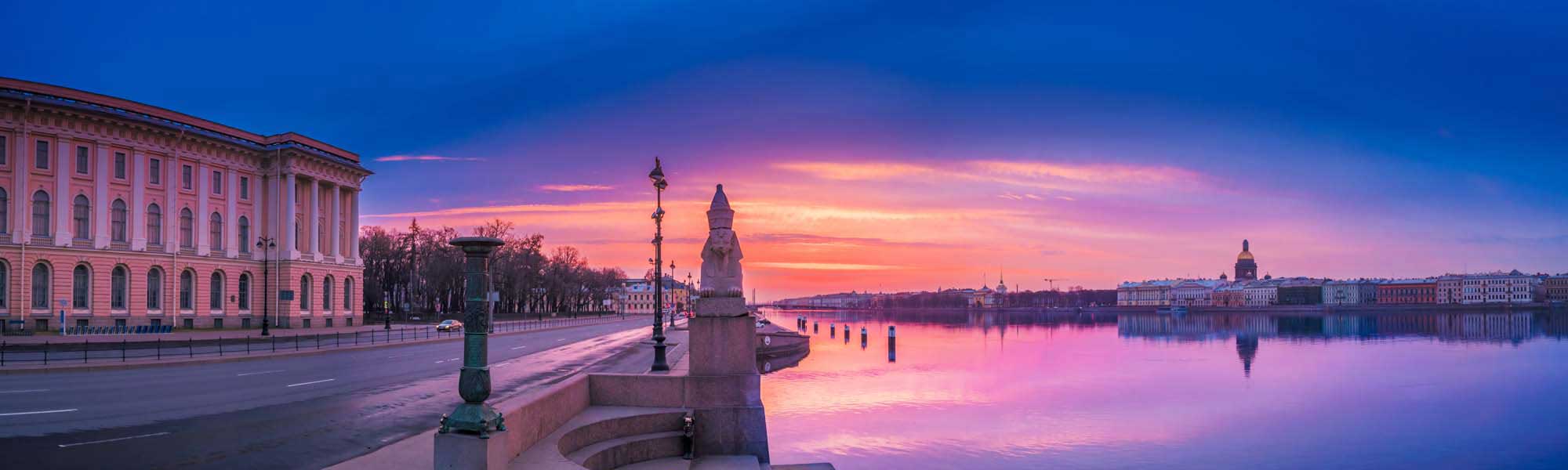 Saint Petersburg Sunrise Over the Neva River A breathtaking dawn scene over the Neva River in Saint Petersburg, Russia, featuring the iconic pink neoclassical building on the left, ornate lamp posts, and the city's historic skyline reflected in the calm water under a vibrant purple and orange sunrise sky.