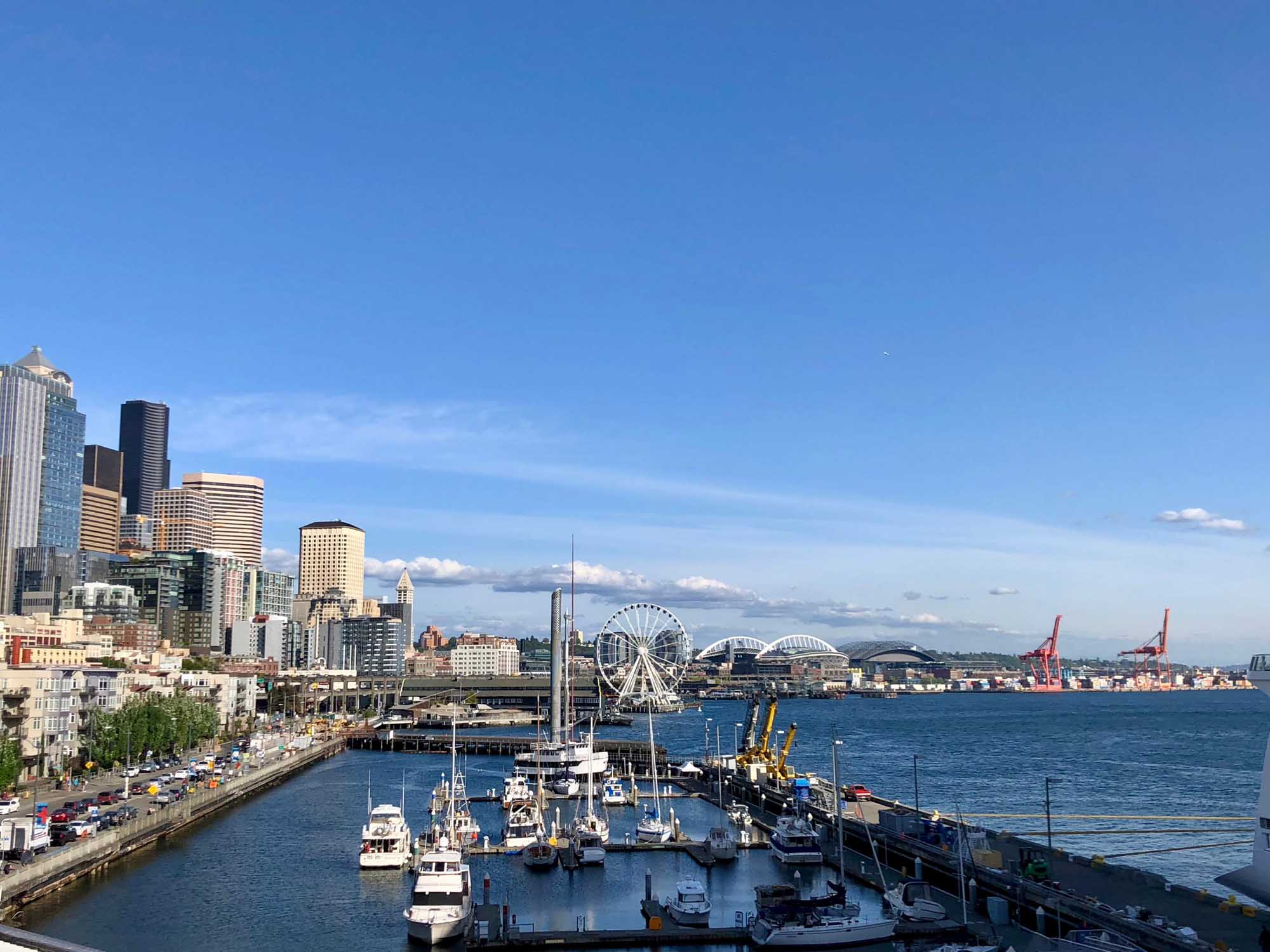 Seattle Waterfront and Harbor District A panoramic view of Seattle's downtown skyline and waterfront featuring the iconic Space Needle, the Seattle Great Wheel, and numerous moored vessels in Elliott Bay. The image captures the bustling port district with modern skyscrapers, historic buildings, and the pristine blue waters of Puget Sound under clear skies.