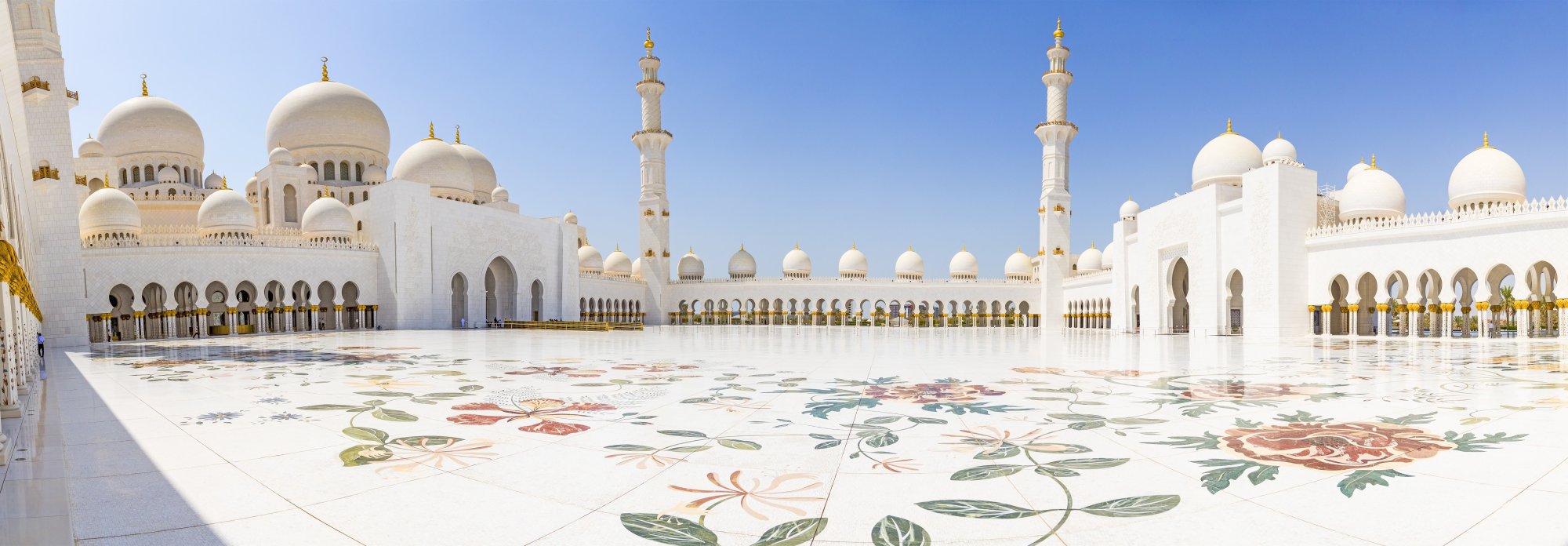 Sheikh Zayed Grand Mosque Courtyard A stunning view of the Sheikh Zayed Grand Mosque in Abu Dhabi, featuring its iconic white marble architecture with golden domes and minarets, ornate floral marble inlay patterns covering the vast courtyard floor, and pristine Islamic geometric design elements under clear blue skies.