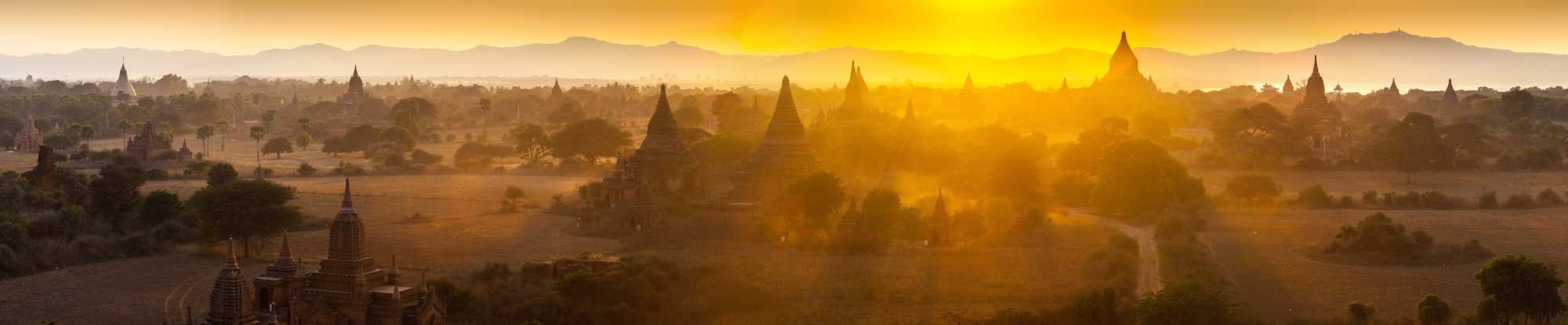 Sunset Over Bagan Temple Complex A breathtaking panoramic view of thousands of ancient Buddhist temples silhouetted against a golden sunset in Bagan, Myanmar. The landscape is bathed in warm amber light with misty atmospheric haze obscuring the lower valleys, creating a mystical and timeless scene of this UNESCO World Heritage Site.