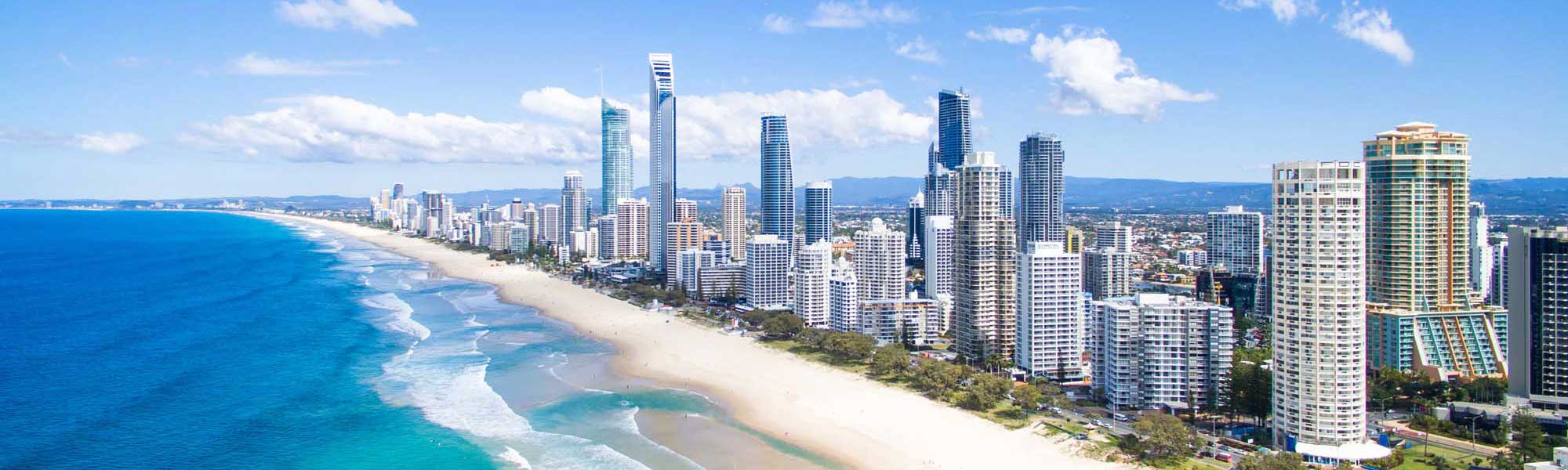 Surfers Paradise Beach Skyline Gold Coast An aerial view of Australia's Gold Coast featuring a stunning high-rise beachfront skyline with modern condominiums and hotels lining pristine golden sand beaches adjacent to sparkling turquoise ocean waters with white-capped waves.