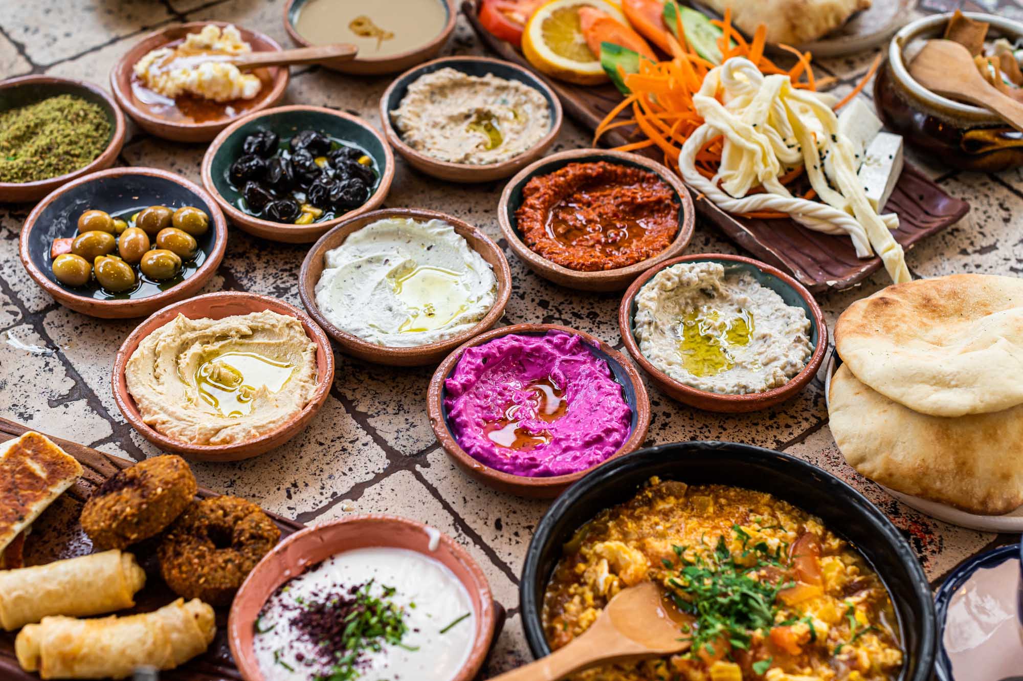 Traditional Turkish Family Breakfast Spread A vibrant overhead spread of authentic Turkish breakfast featuring various mezze dips including hummus, baba ganoush, and muhammara in terracotta bowls, accompanied by fresh vegetables, olives, pastries, bread, and traditional accompaniments artfully arranged on a rustic surface.