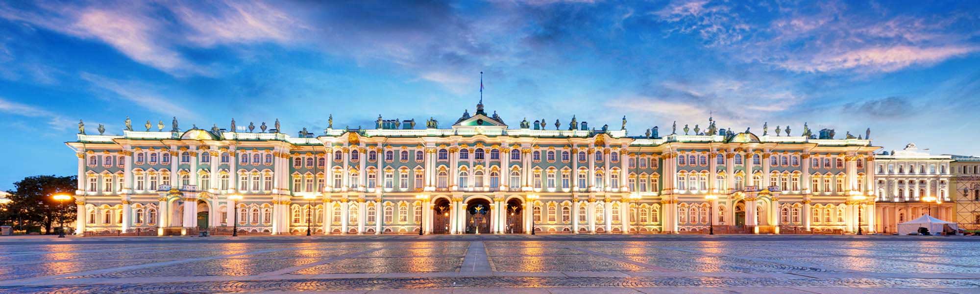 Winter Palace at Palace Square, Saint Petersburg The iconic Winter Palace illuminated at dusk, showcasing its distinctive pink and white Baroque architectural facade across Palace Square in Saint Petersburg, Russia. The grand 18th-century imperial residence reflects warm golden light on the wet plaza surface beneath a blue twilight sky.