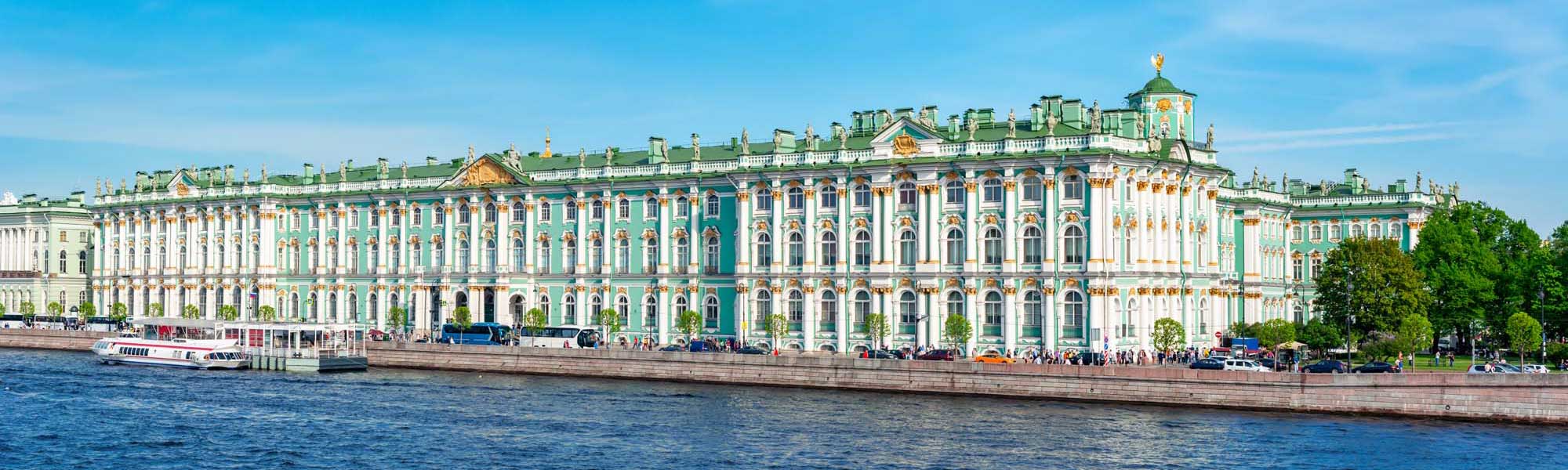 Winter Palace on the Neva River The magnificent Winter Palace in St. Petersburg, Russia, displaying its iconic turquoise and white Baroque façade with golden ornamental details, as viewed from the Neva River. The grand 18th-century imperial residence features multiple stories of arched windows, decorative moldings, and a distinctive green roof punctuated by ornamental spires.