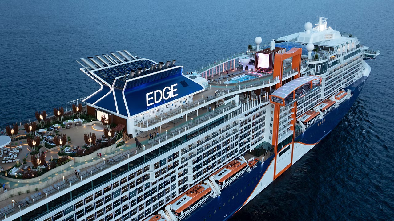 A modern luxury cruise ship sails peacefully through calm tropical waters during a spectacular golden sunset, with vibrant orange and pink clouds reflected on the sea's surface. The vessel's contemporary design and white superstructure are illuminated by the warm evening light.